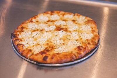 A white pizza with dollops of ricotta, garlic and herbs on a round tray
